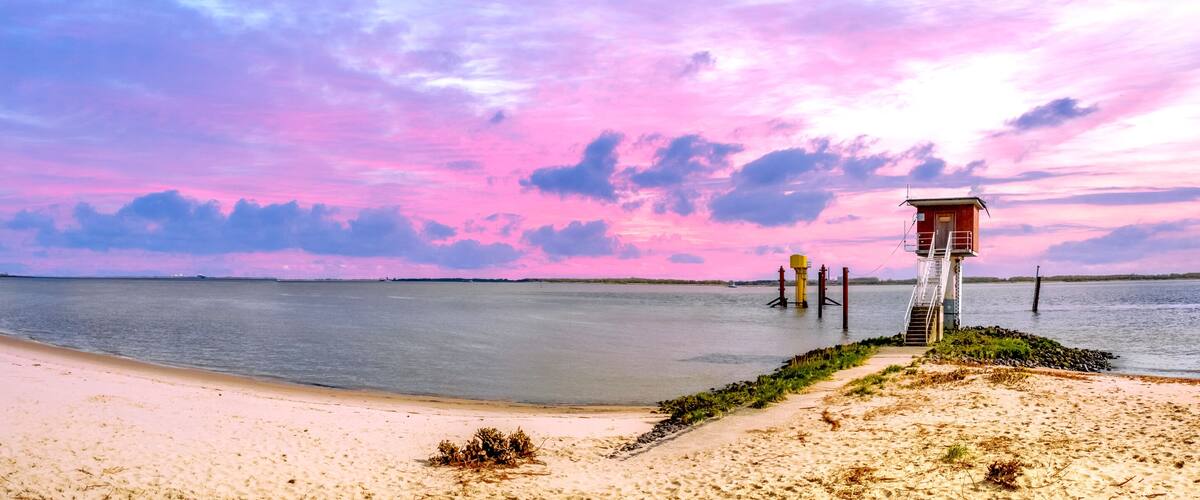 A beach with a pier extending into the water, surrounded by a pink and purple sky.