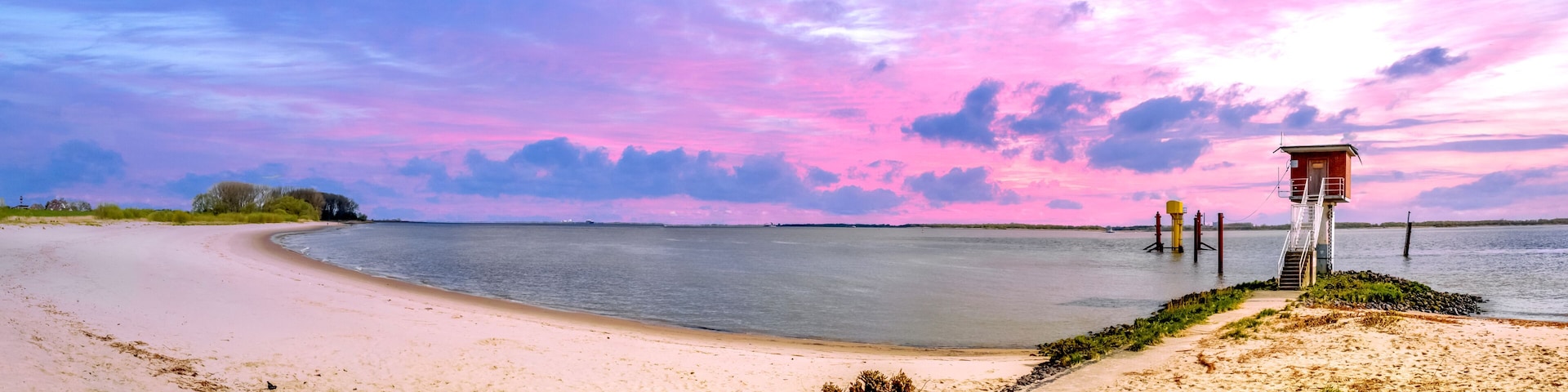 A beach with a pier extending into the water, surrounded by a pink and purple sky.