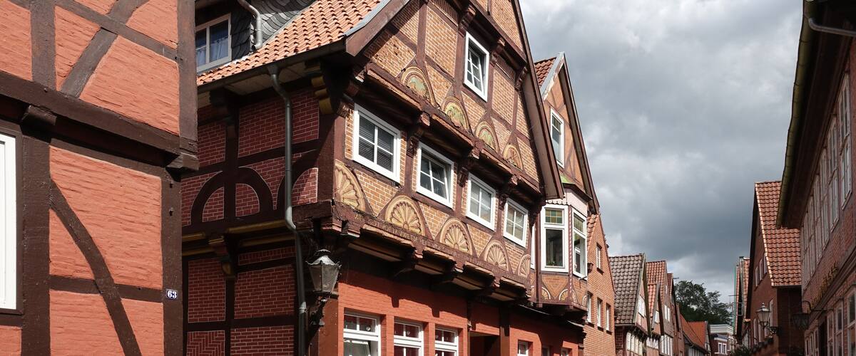 A narrow street lined with traditional half-timbered houses with red brick walls and white window frames.