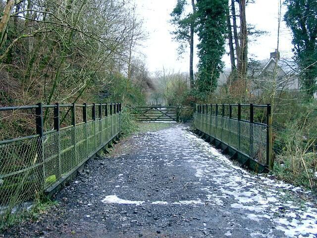 A gravel path leading to a metal gate, surrounded by trees and a fence.