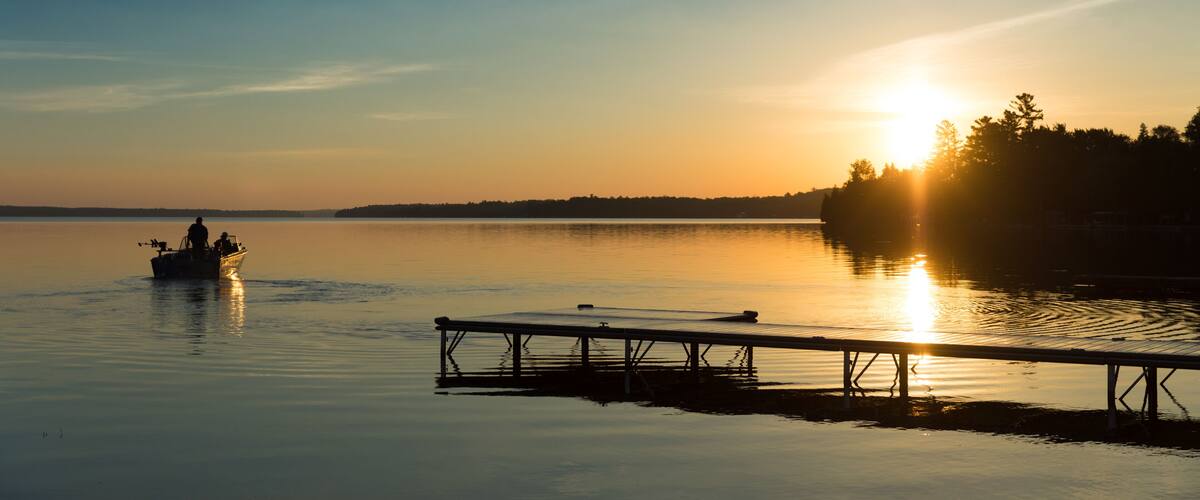 A calm lake at sunset with a boat and dock.