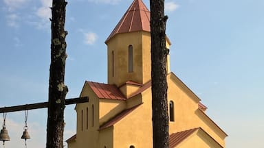 A church with a red roof and a bell tower, surrounded by trees and a fenced area.