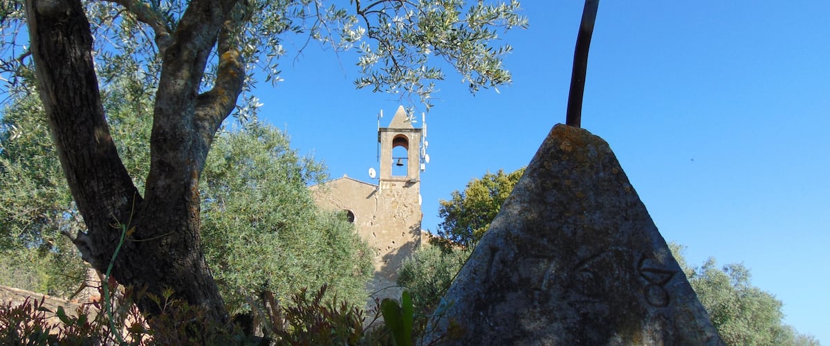 A stone cross, olive trees, and a church tower.