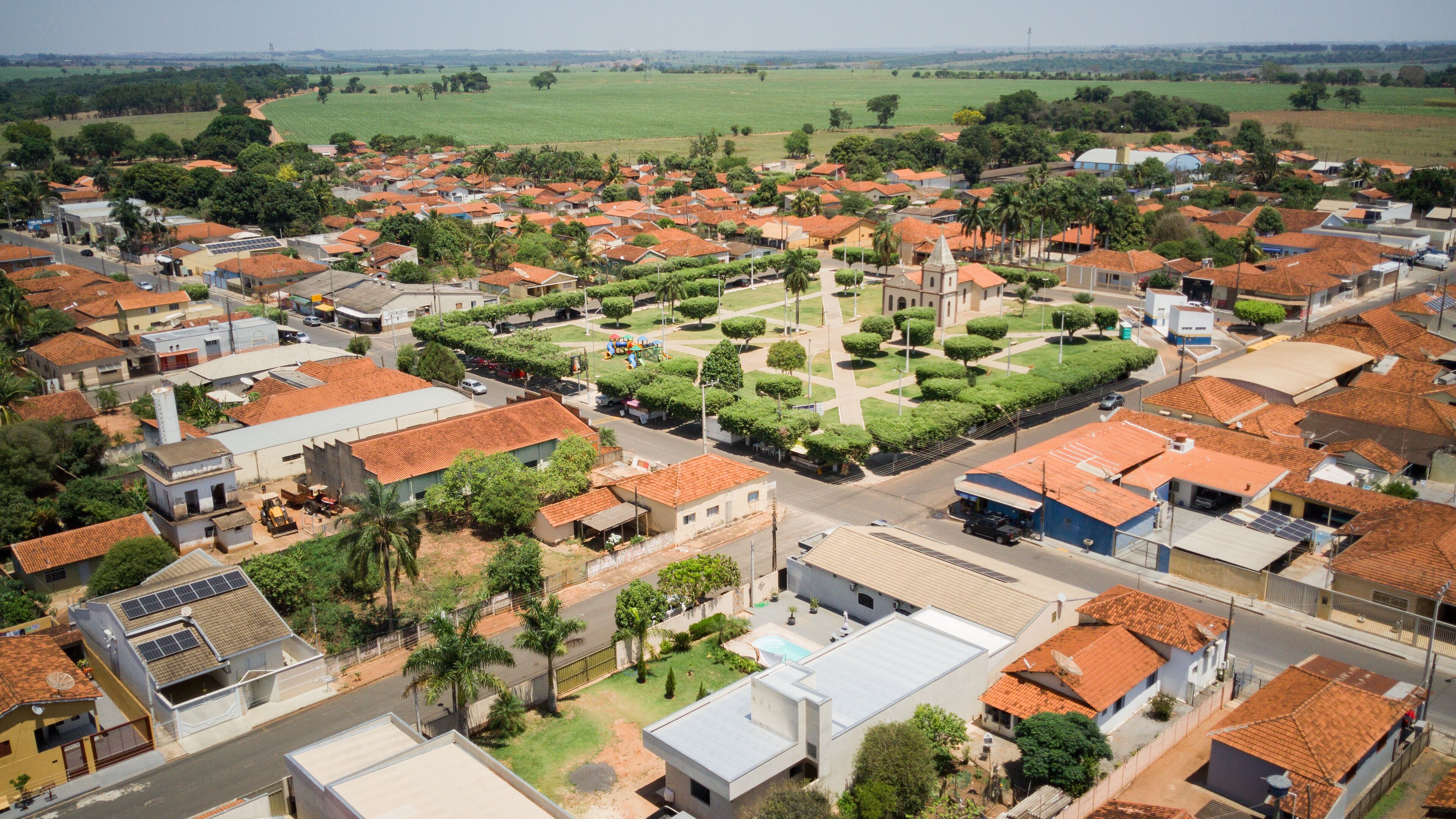 A residential area with red-tiled roofs, green fields, and a central square with a church.