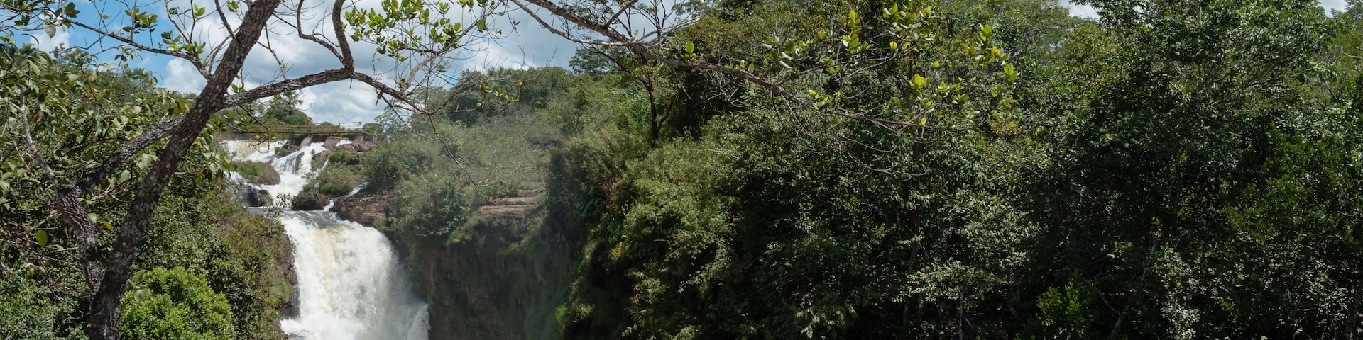 Uma cascata rodeada por uma floresta verde densa e um céu azul límpido.