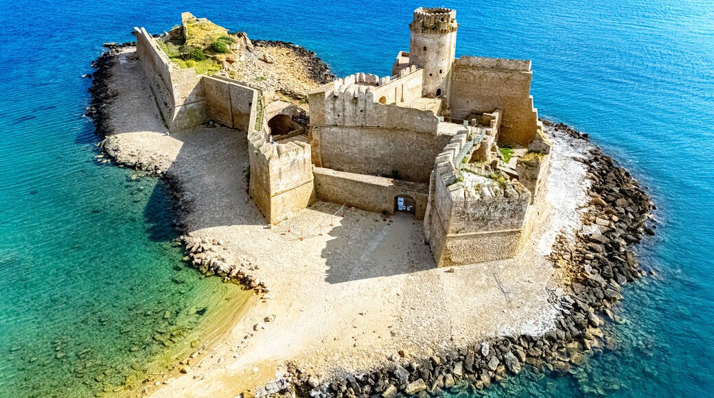 A coastal fortress with a tower, surrounded by clear blue waters and rocky terrain.