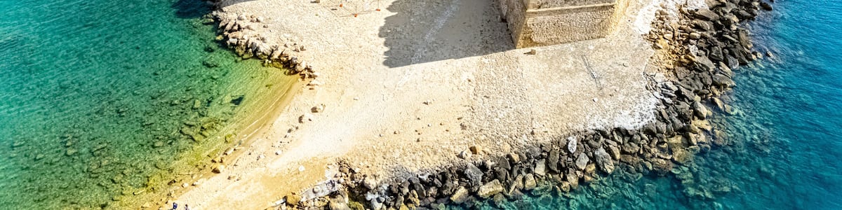 A coastal fortress with a tower, surrounded by clear blue waters and rocky terrain.