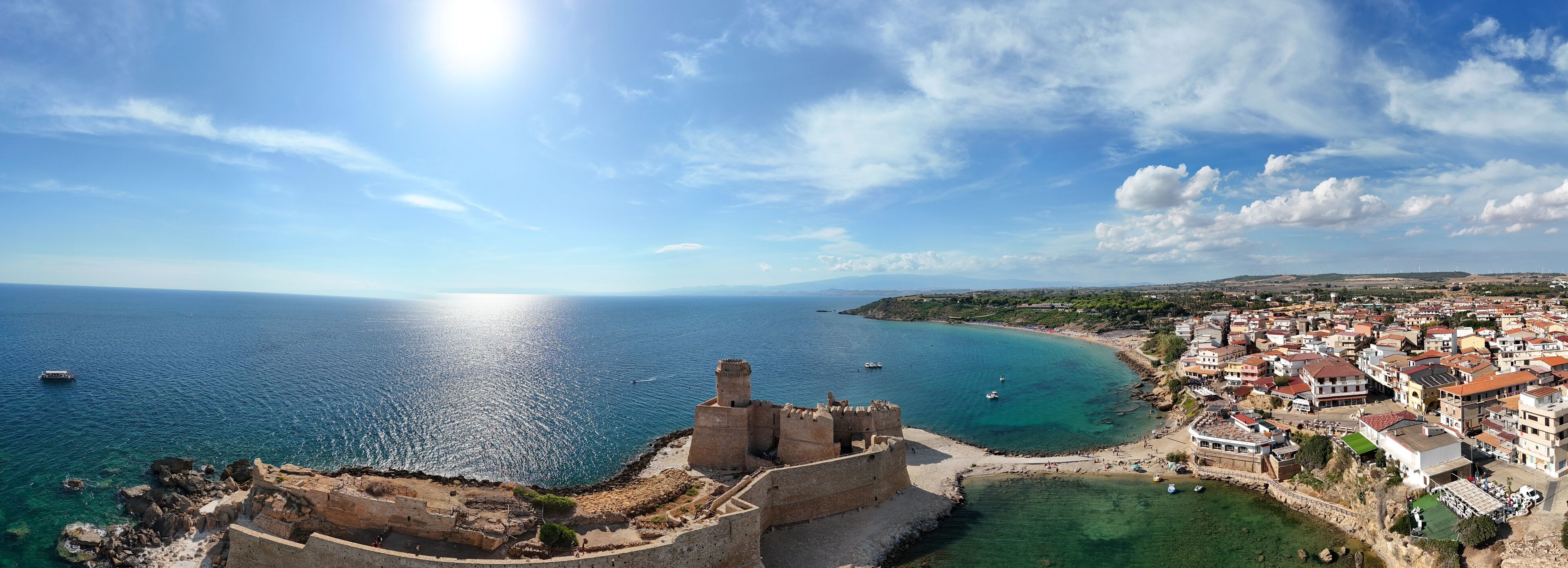A coastal town with a historic fort overlooking the sea, surrounded by residential buildings and a clear sky.