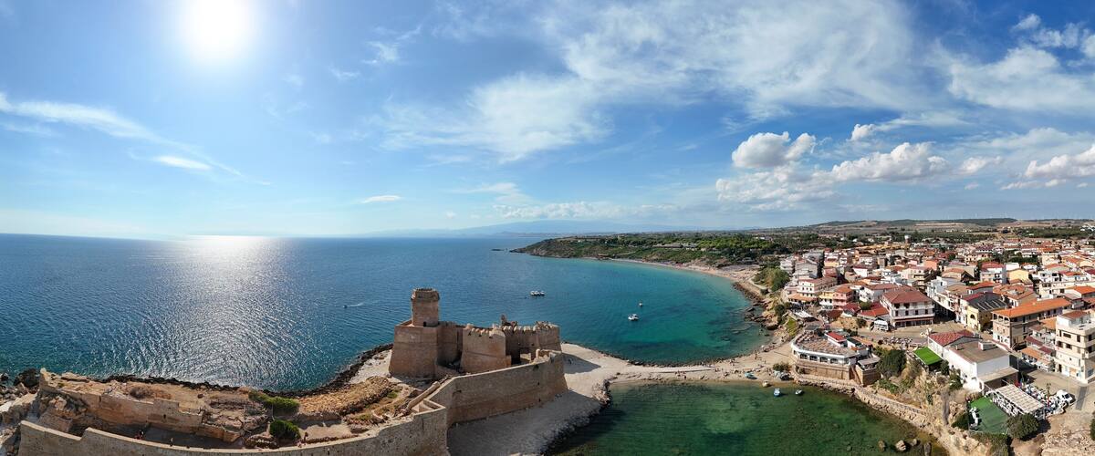 A coastal town with a historic fort overlooking the sea, surrounded by residential buildings and a clear sky.