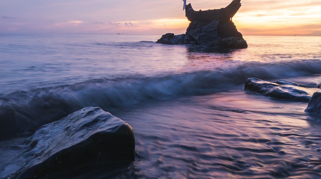 View of the serene beach where water meets the shore, with rocks and a captivating sunset painting the sky with hues of pink and purple, Tejakula, Bali, Indonesia.