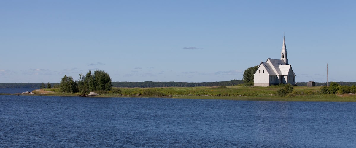 A white church with a steeple on a small island in a body of water.