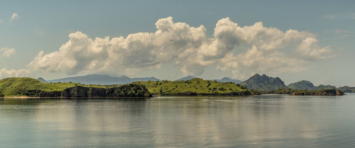 A calm lake with green hills and mountains in the background.