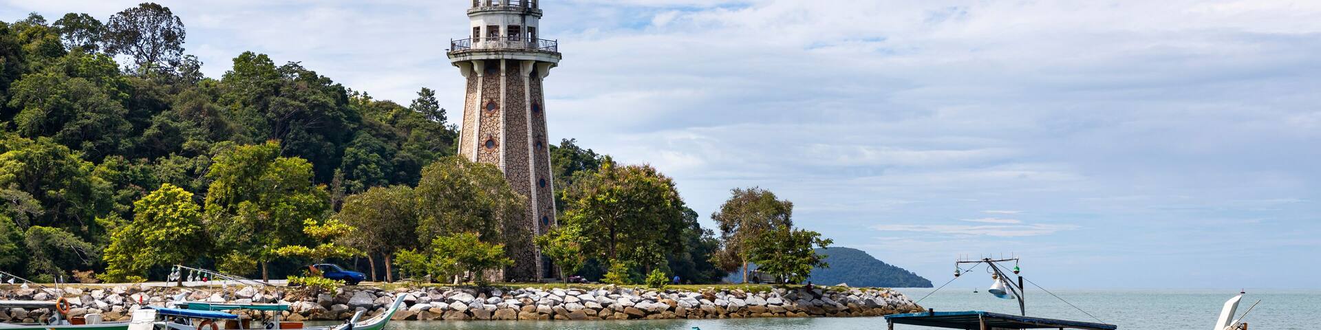 View of perdana quay with a lighthouse and boats by the serene coast, Kuala Teriang, Malaysia.