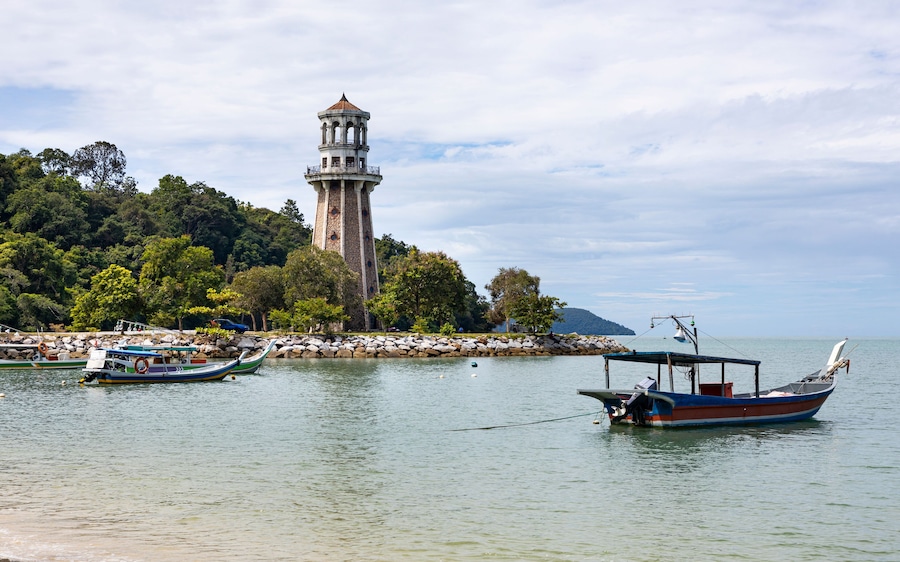 View of perdana quay with a lighthouse and boats by the serene coast, Kuala Teriang, Malaysia.