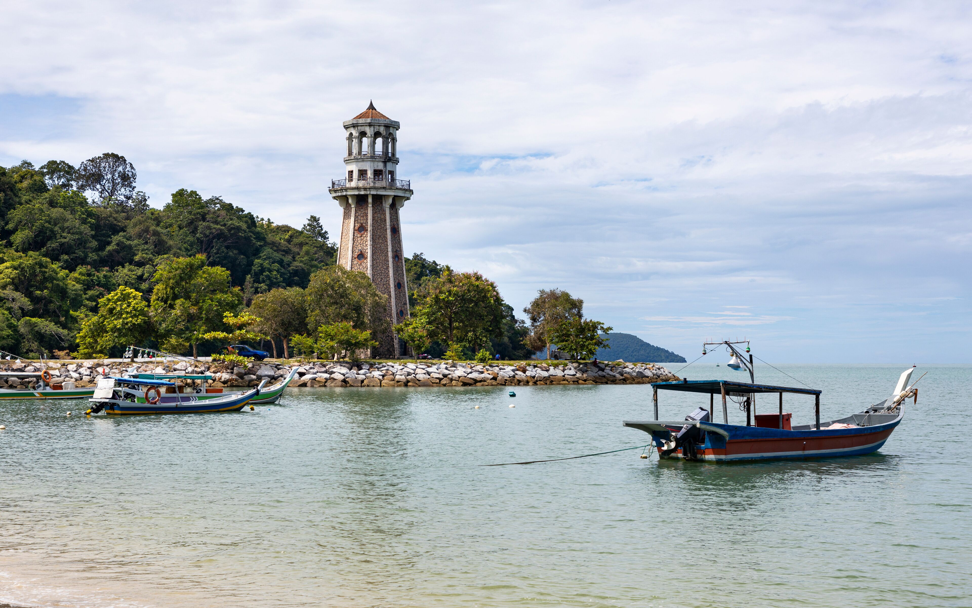 A coastal scene with a lighthouse, boats, and lush greenery.