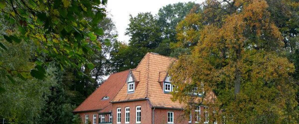 A red brick house with a tiled roof, surrounded by a green lawn and trees.