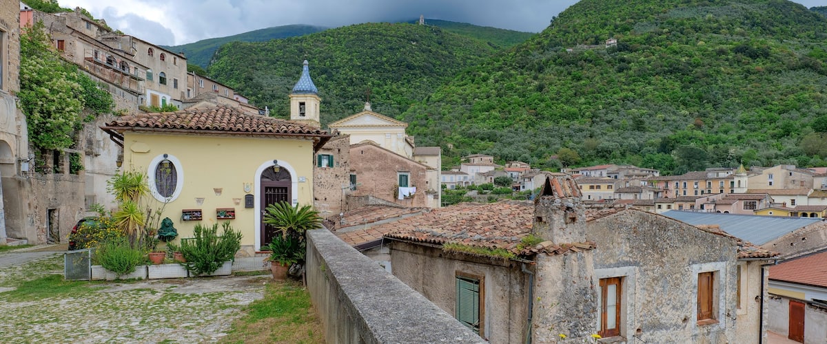 A hillside village with terracotta-roofed buildings, a church with a bell tower, and lush green hills in the background.