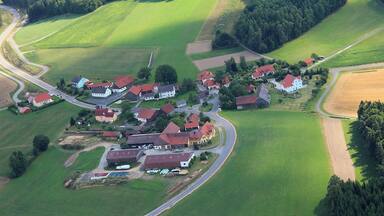 Vista aérea de uma aldeia rural com casas, estradas, campos e florestas.