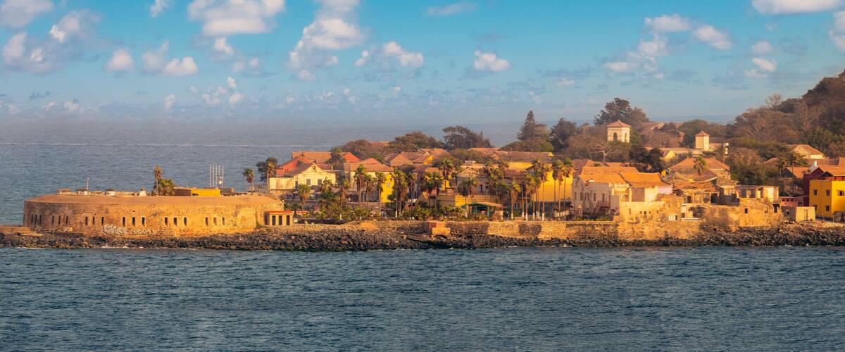 A coastal town with a fortified structure, colorful buildings, and a clear view of the sea.