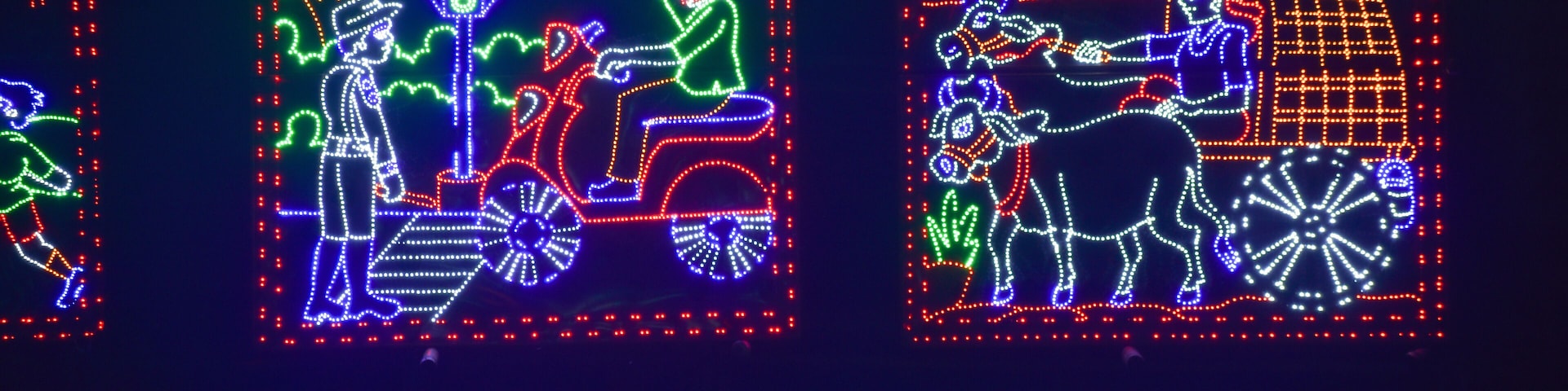 Letreros de neón iluminados que muestran a un hombre en motocicleta y a otro con un carruaje tirado por caballos.