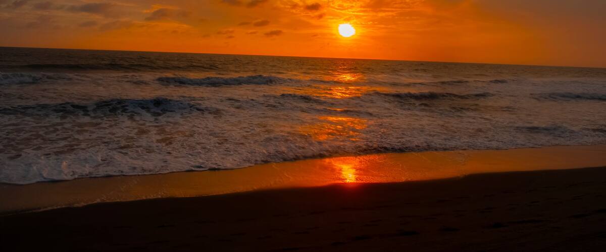 A sunset over the ocean with waves crashing onto the shore.