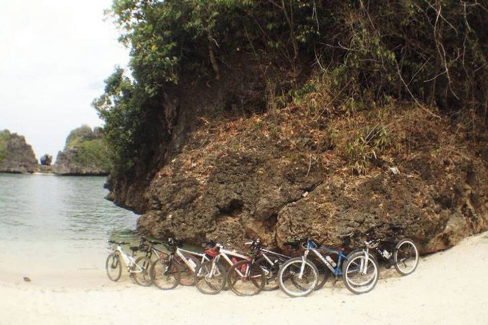 Des vélos sont garés sur une plage de sable, à côté d’une falaise rocheuse, au bord de l’eau.