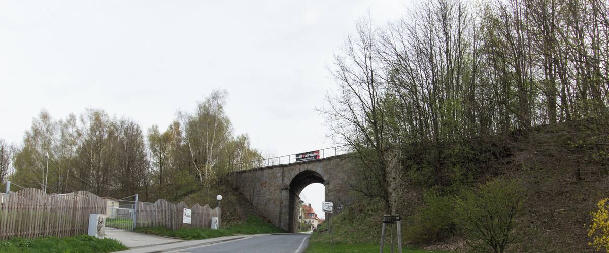 A paved road leading to a stone bridge with a sign above it.