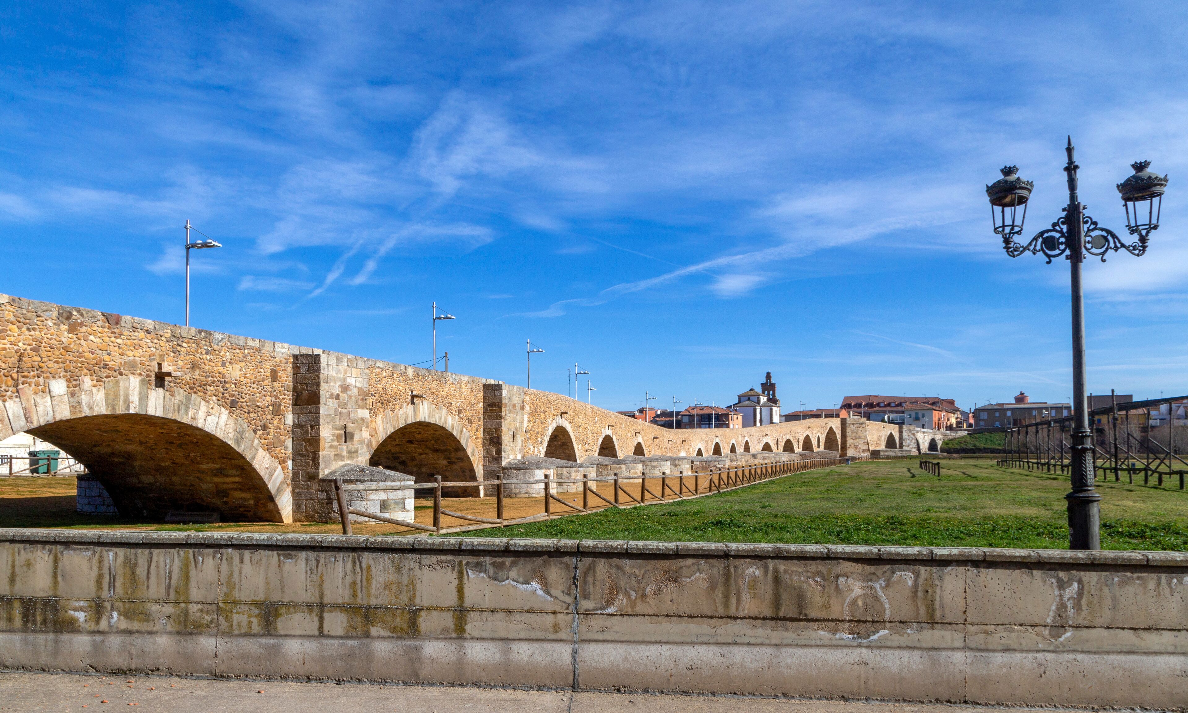 A stone bridge with multiple arches, a grassy area, and a street lamp.