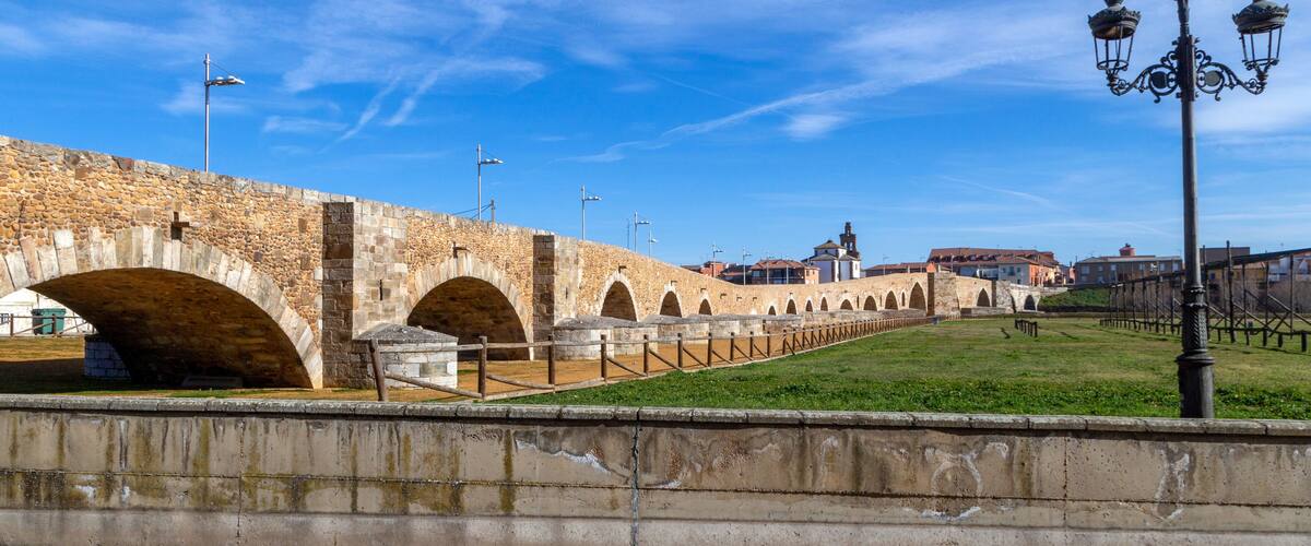 A stone bridge with multiple arches, a grassy area, and a street lamp.