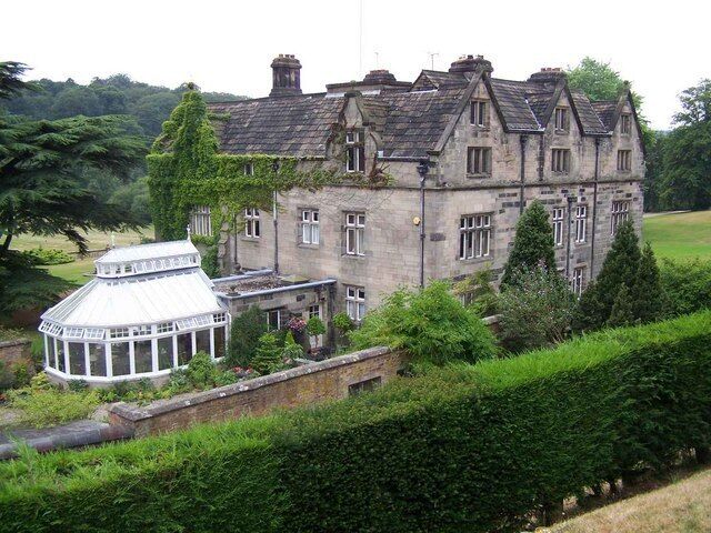 A large stone building with a glass conservatory, surrounded by lush greenery.
