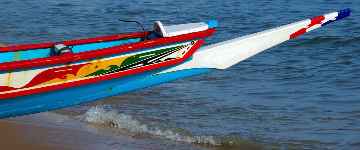 A colorful boat with a red, white, and blue tail fin resting on a sandy beach.