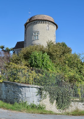 A historic tower with a round base and a conical roof, surrounded by lush greenery and a stone wall.