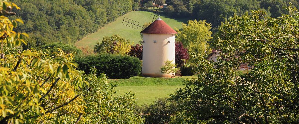 A tower with a red roof surrounded by lush greenery and hills in the background.