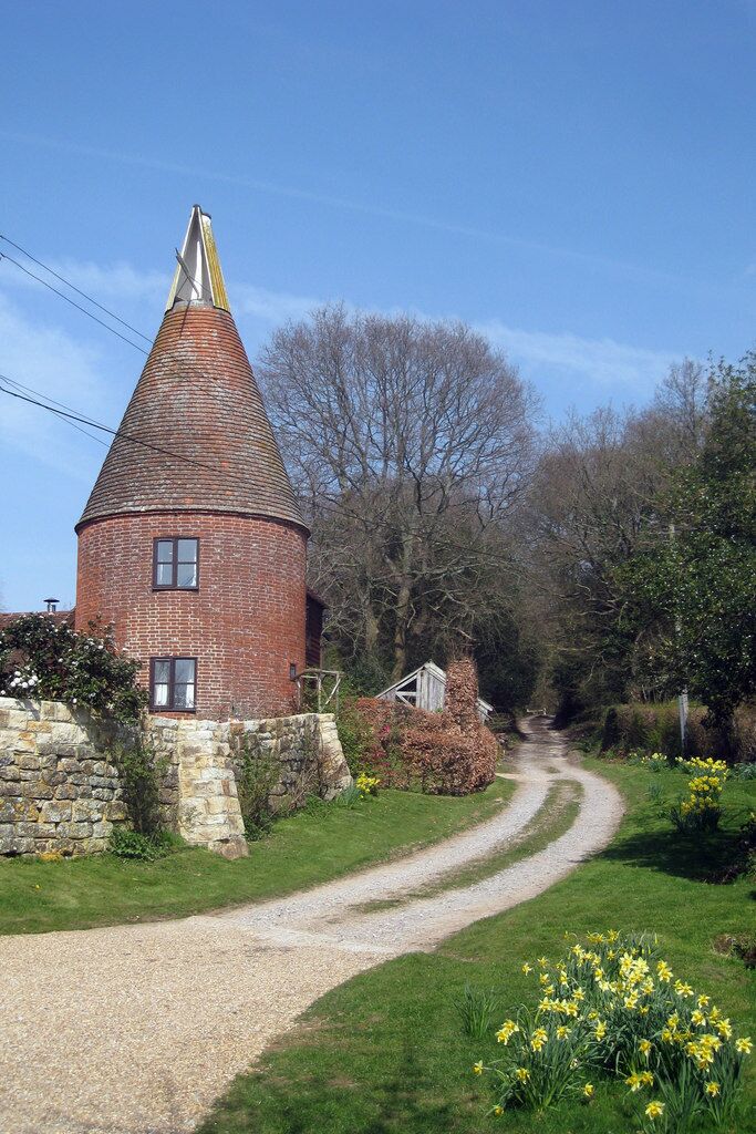 A brick tower with a conical roof, a gravel path, and daffodils in the foreground.