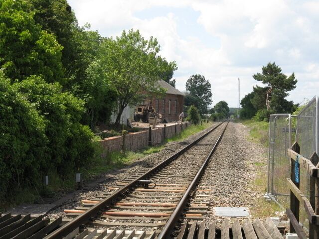 Railway tracks with a brick building and trees in the background.