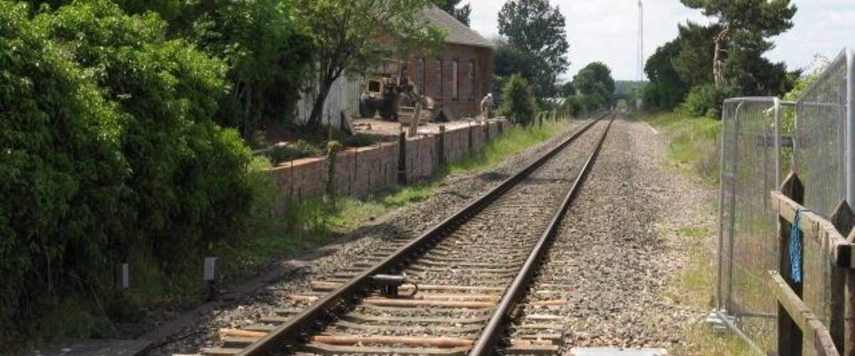 Railway tracks with a brick building and trees in the background.