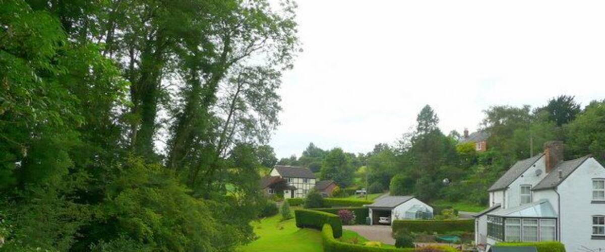 A lush green garden with a pathway, white houses, and a small pond.