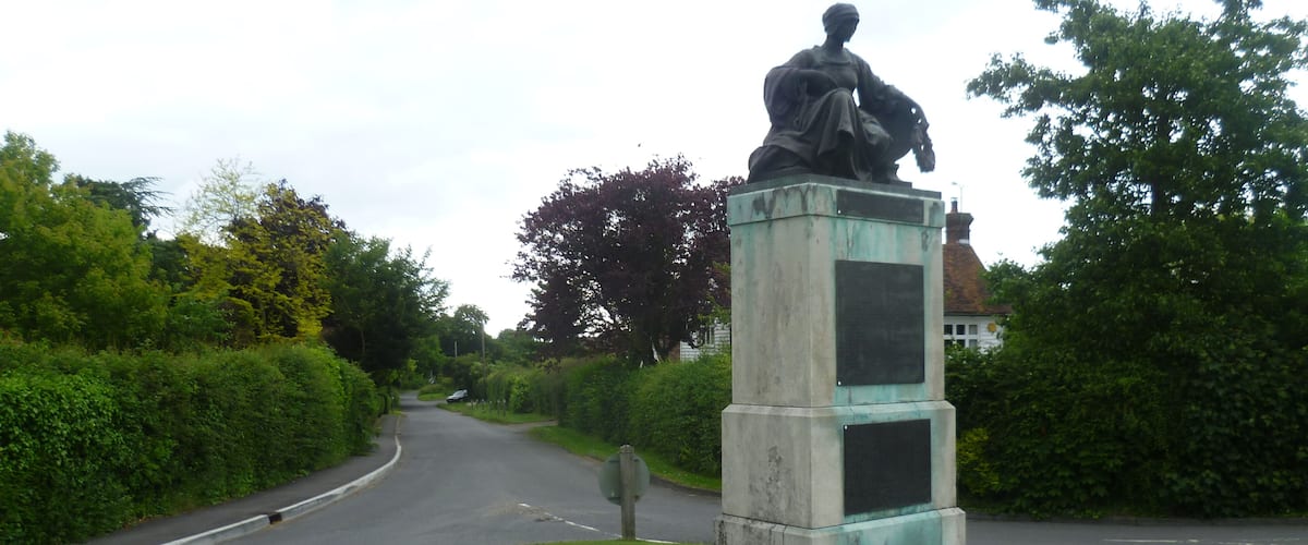 A statue on a pedestal in a grassy area beside a road.