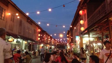 A bustling street at dusk with string lights and lanterns, wooden buildings, and people dining.