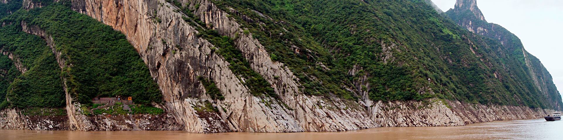 A mountainous landscape with steep cliffs and a river at the base.