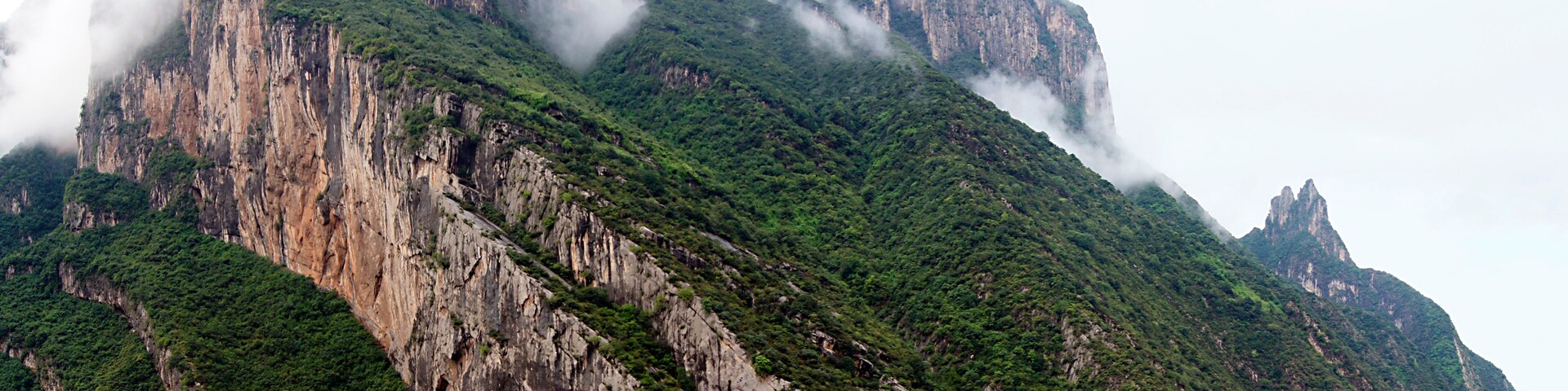 Paisagem montanhosa com penhascos íngremes e um rio na base.