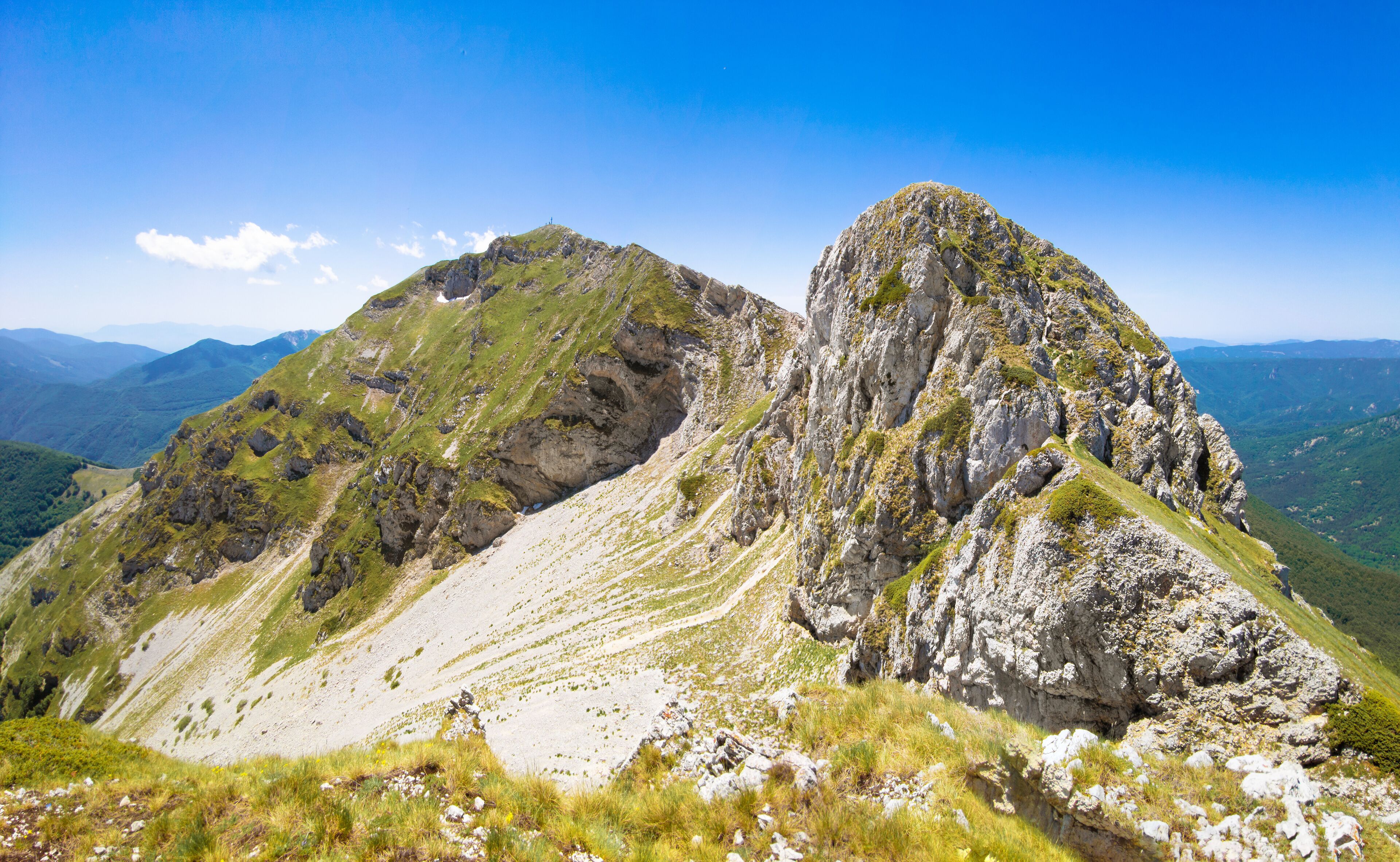 A rugged mountain landscape with rocky peaks and grassy slopes under a clear blue sky.