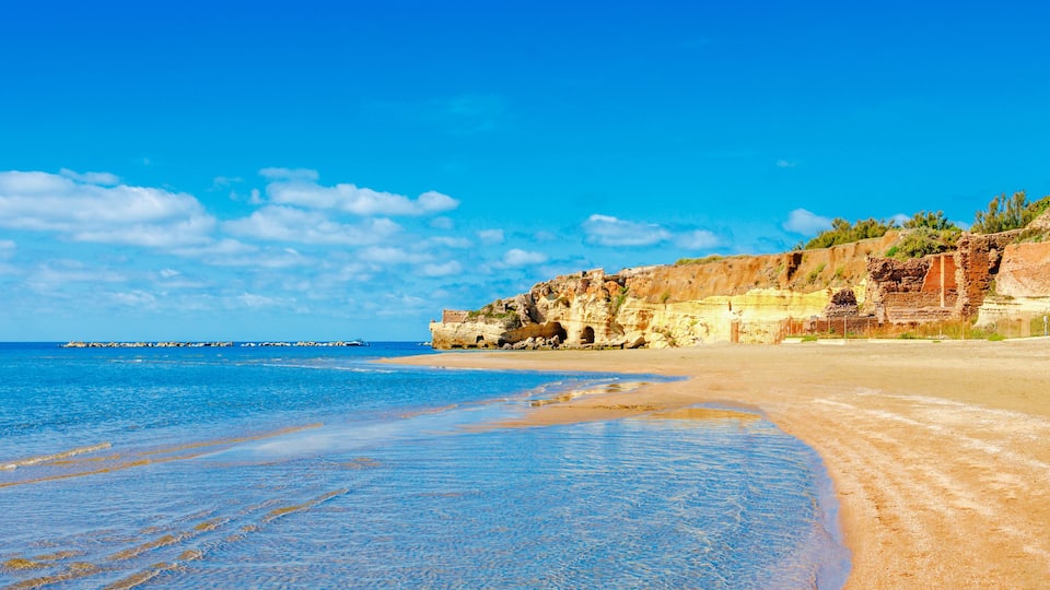 A beach with clear blue water, sandy shore, and rocky cliffs.