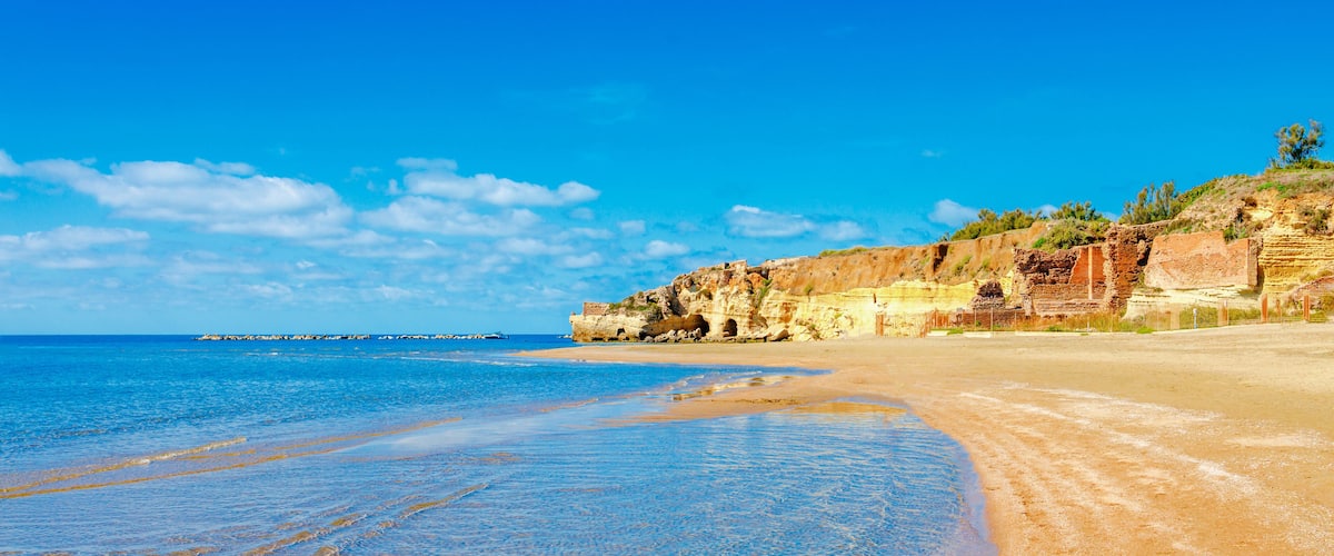 A beach with clear blue water, sandy shore, and rocky cliffs.