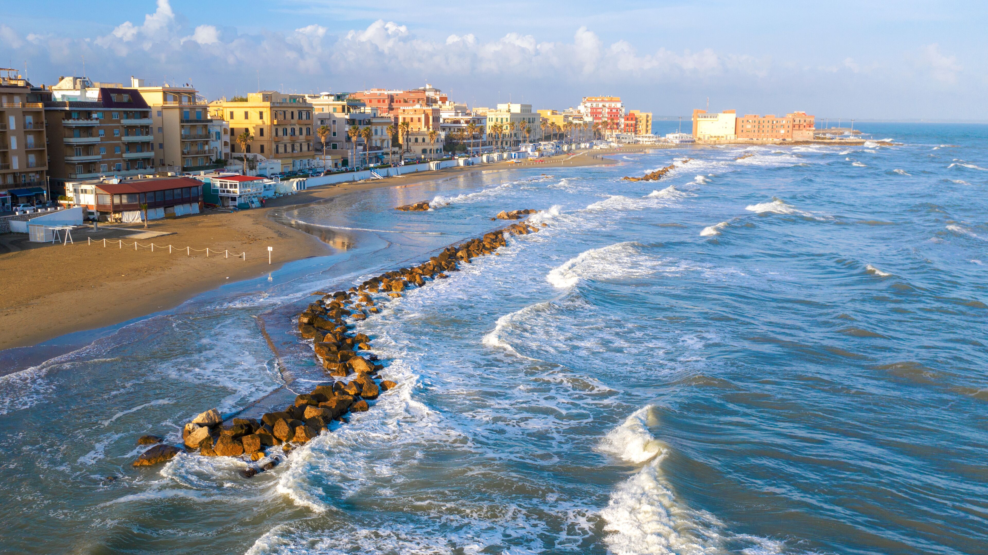 Aerial view of the coast of Anzio, a small sea town near Rome, in Italy. There is no one on the beach on this cold spring day. The blue sea with its waves is rough. In the sky there are some clouds.