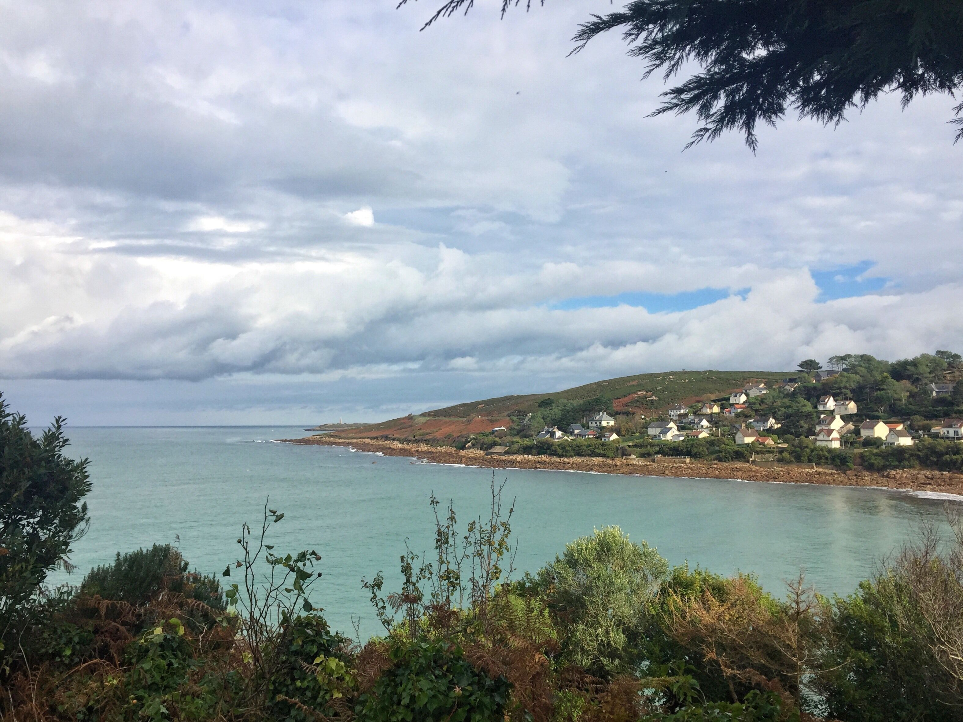 A coastal landscape with houses on a hillside, a body of water, and overcast skies.