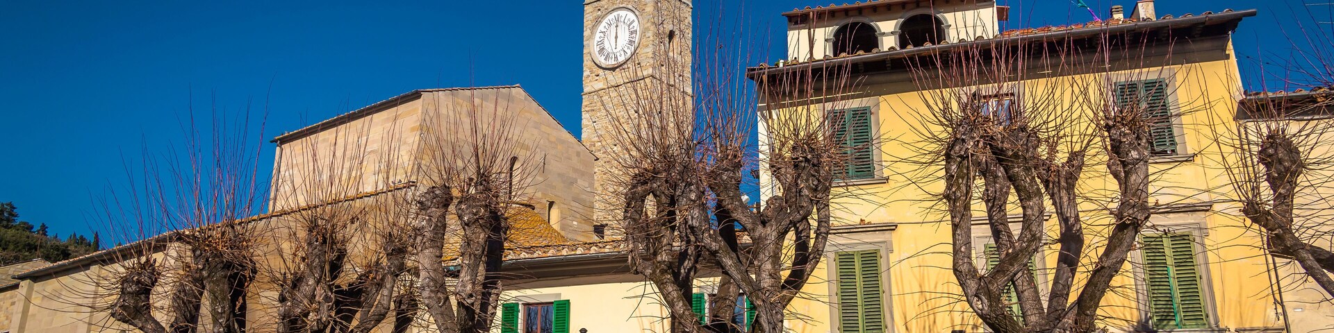 Un edificio histórico con una torre del reloj, árboles y una calle con motocicletas estacionadas.