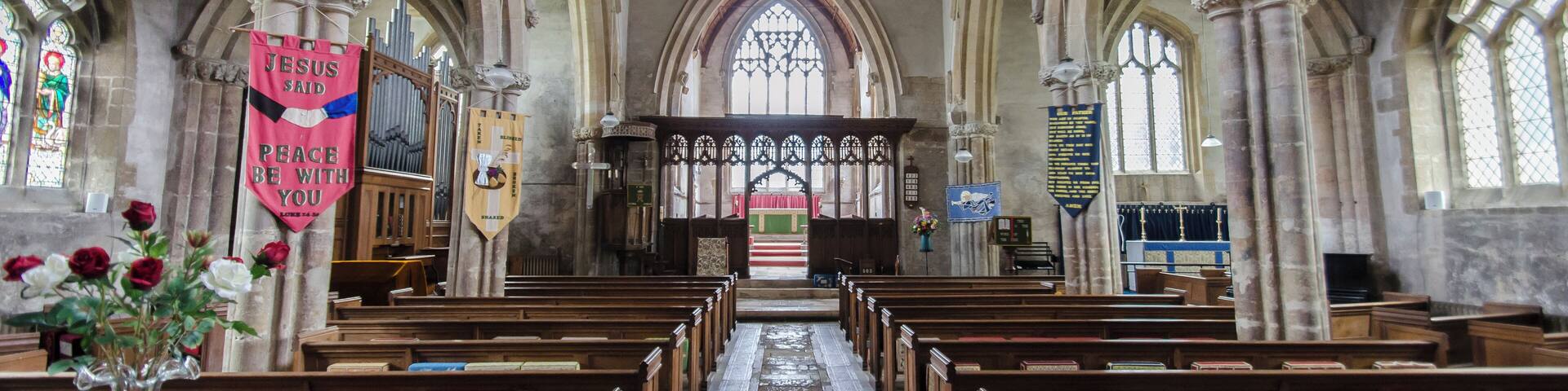 The church dates from circa 1300, and is built from ashlar with the lead roofs. The church is a cruciform plan with a west tower and spire, nave with north and south aisles, south porch, transepts, chancel and north vestry. The tower is of four stages, the two lower of circa 1300, the two upper of circa 1500. On the east side of the nave the original steeply pitched roofline is visible. The tower has ornate pinnacles and projecting gargoyles, the octagonal spire is 15th century with lucarnes, Crockets and finial. The nave has clerestory windows of three lights. There are moulded eaves with corbel heads above,and a frieze of shields, battlements and ornate pinnacles. The north aisle has an early 14th century west window and on the roof is a small bell turret,the north transept has early 14th century window of three lights. The chancel is 15th century and was restored in the 19th C. It has two large windows on both north and south sides each of three lights. There are hood moulds and grotesque animal label stops.There is a large pointed east window of five lights with perpendicular tracery. The original roofline of the chancel is visible on the east end of the nave. The south transept was probably remodelled in the 15th century from a detached lady Chapel built circa 1275. The west side of the transept has 14th century windows with head label stops. The porch is 14th century and has 15th century ornamentation, it has projecting gargoyles and ornate pinnacles. It contains stone benches and a corbel that once supported a roof, one is dated 1631. The 14th century west door has foliated capitals with elaborate finials. The nave has three bays, with piers from circa 1300. The south wall of the south transept has three 13th century sedilia and two aumbries. The chancel arch is from the 14th century and has caryatid figures. There is a 14th century screen which was restored in the 19th century. There is a 14th century hexagonal font with ornate Gables and pinnacles. The church contains various small 18th and 19th-century monuments. The church has recently undergone much restoration work including work to the spire, tower, bells, roof, windows and a new boiler system.