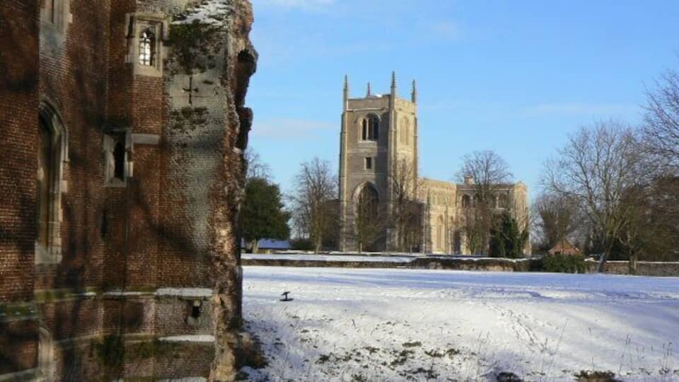 A snow-covered field with a historic brick building and a church in the background.