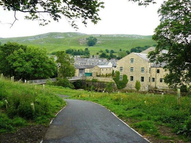 A rural road leading to a stone building surrounded by greenery and hills.